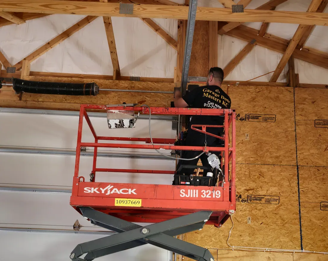 Garage Door Masters KC technician on a lift servicing a large commercial sectional overhead door and its torsion spring in the Kansas City metro